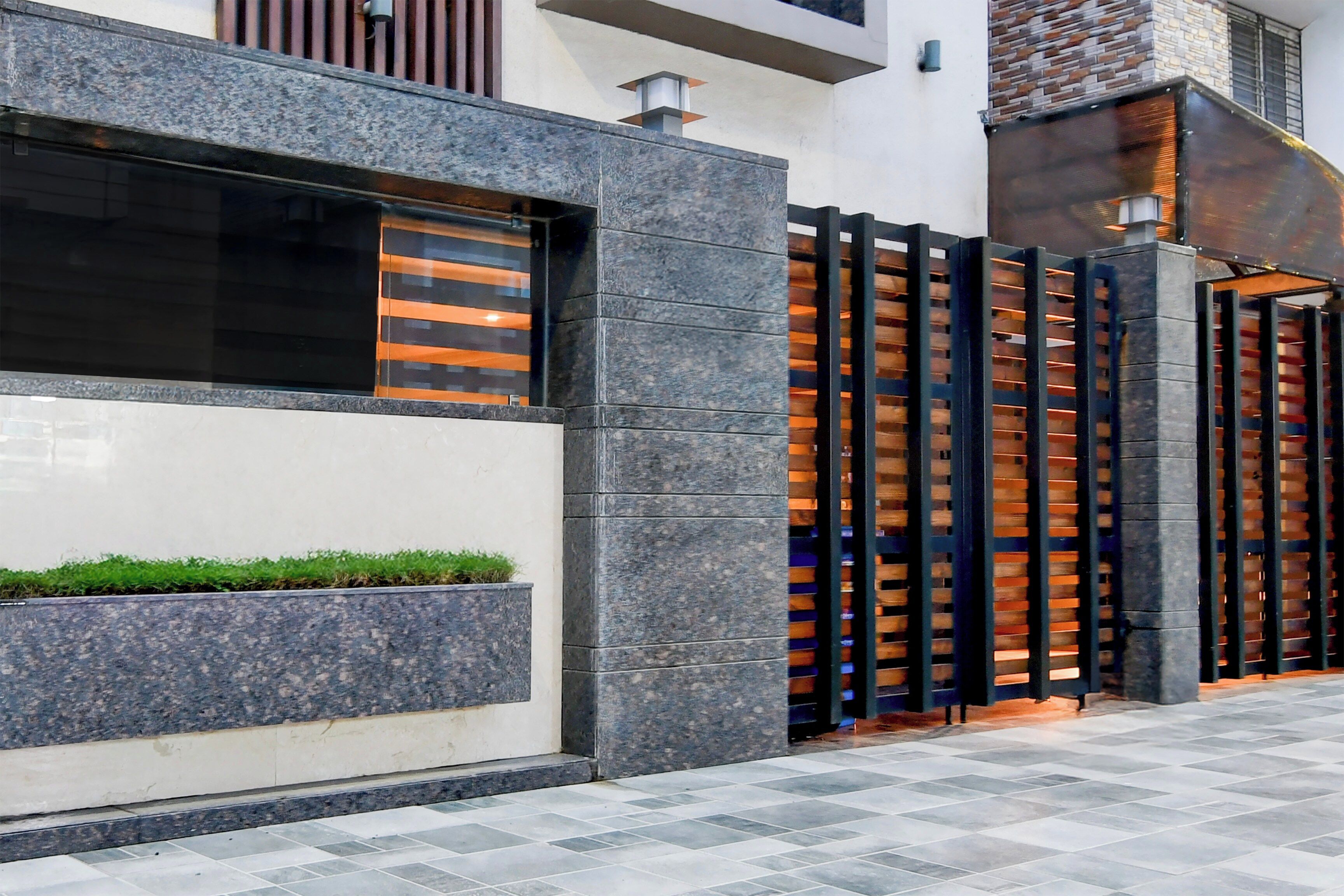 Fachada moderna de edificio con revestimiento de piedra, una reja metálica y una jardinera con césped.
