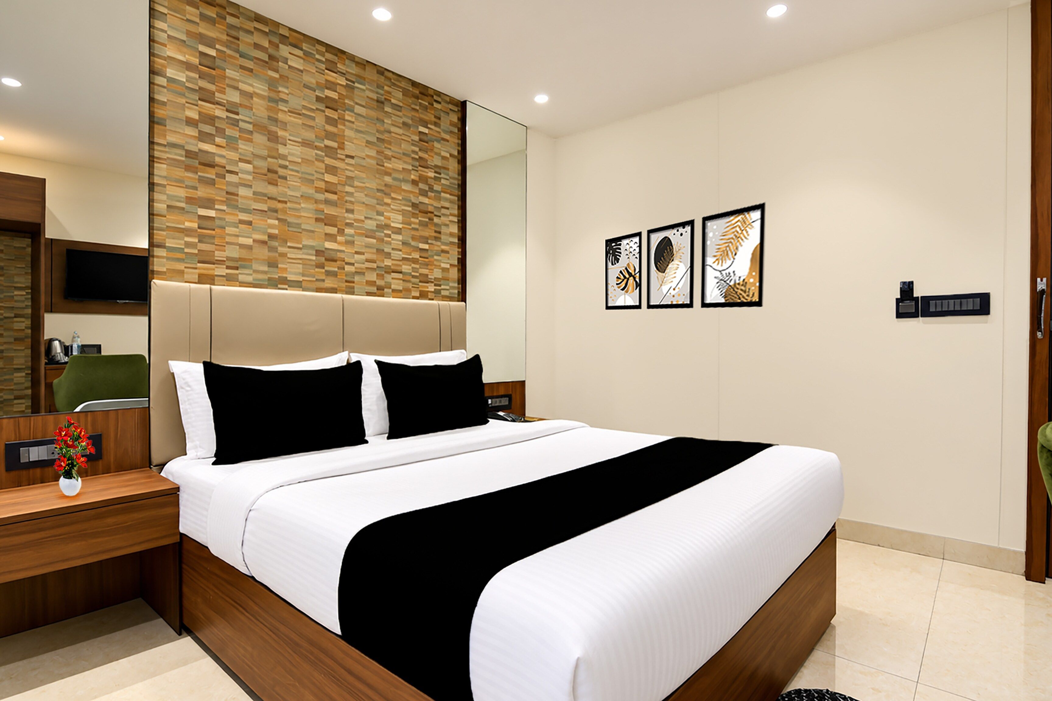 Una habitación de hotel moderna con una cama grande, cabecera de madera, televisor de pantalla plana, mesita de noche con un florero y una obra de arte colgada en la pared.