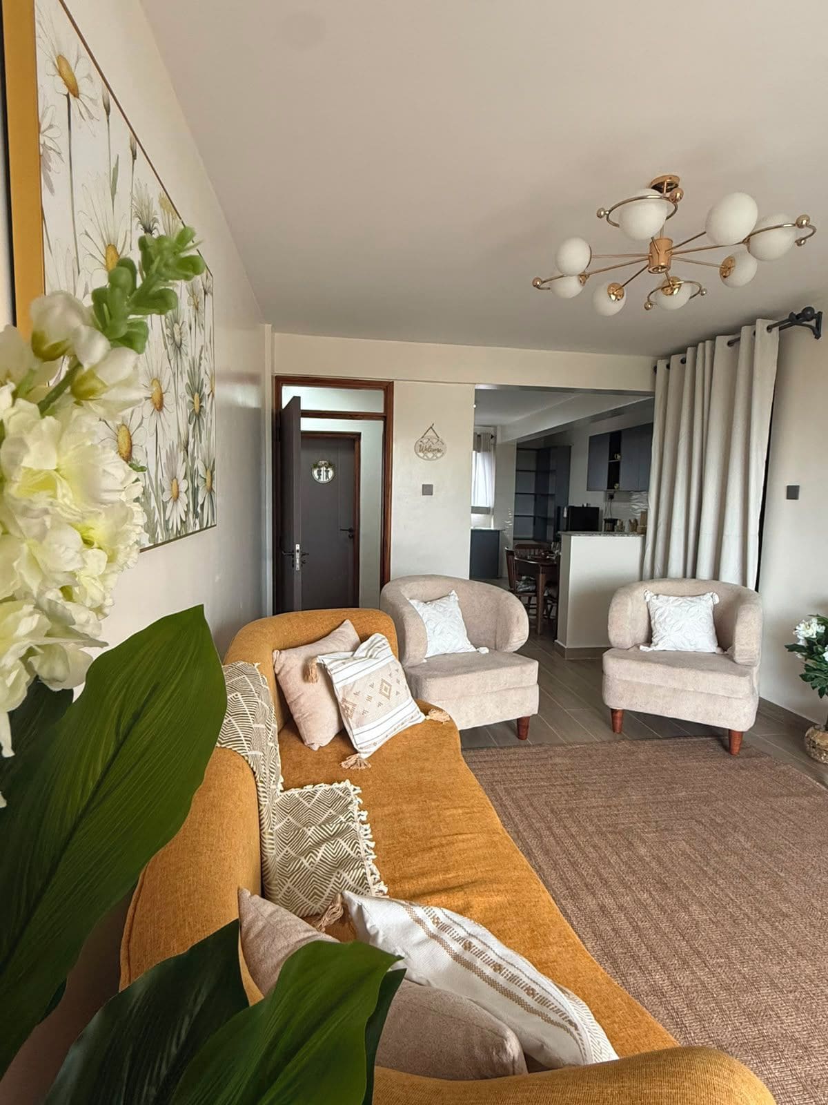 A living room with a sofa, two armchairs, a chandelier, and a door leading to a kitchen.