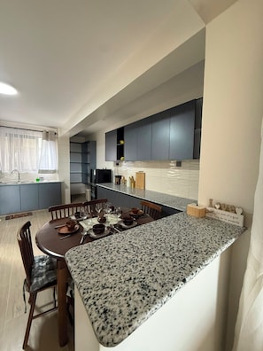 A modern kitchen with dark cabinets, a granite countertop, and a dining area with a table set for four. - Nakuru View Palace Apartment (Nakuru)