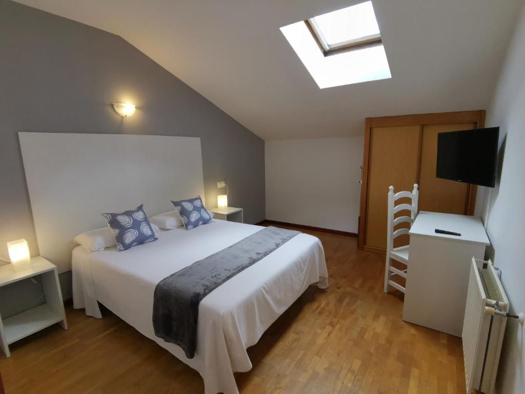 A bedroom with a bed, bedside tables, a TV, a radiator, and a skylight.