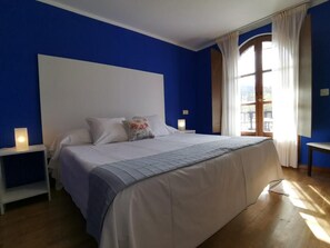 A bedroom with a large bed, two bedside tables, a window with curtains, and a view of the outdoors. - Hotel Trasgu (Cangas de Onís)