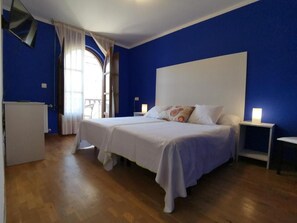 A bedroom with two beds, a white headboard, a bedside table with a lamp, and a window with curtains. - Hotel Trasgu (Cangas de Onís)