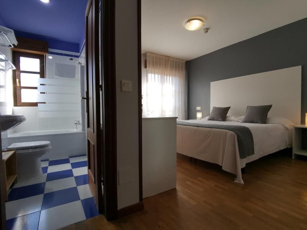 Un dormitori amb llit, taula de nit i finestra amb cortines.