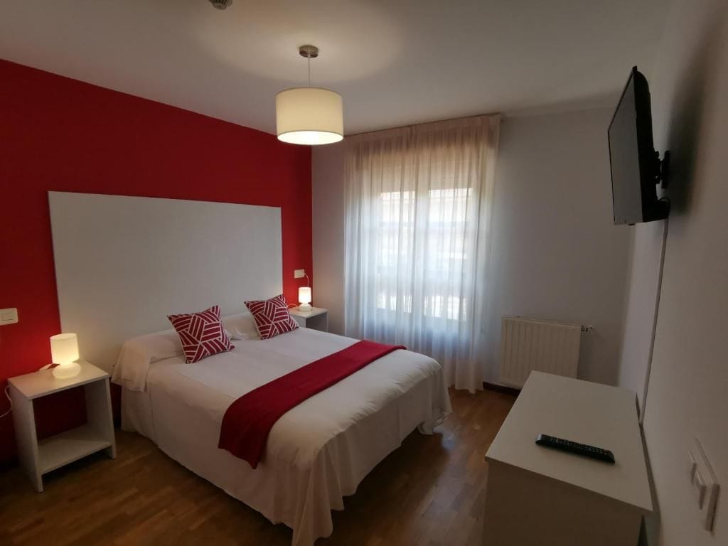 A bedroom with a bed, bedside tables, a TV, and a window with curtains.
