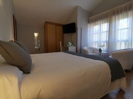 A hotel room with a large bed, a television mounted on the wall, a desk with a chair, and a window with curtains.