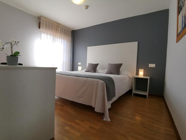 Un dormitorio con cama, mesitas de noche, una planta en maceta y una ventana con cortinas.