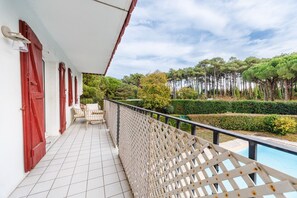 A balcony with a pool, red shutters, and a view of trees and bushes. - New Listing (Anglet)