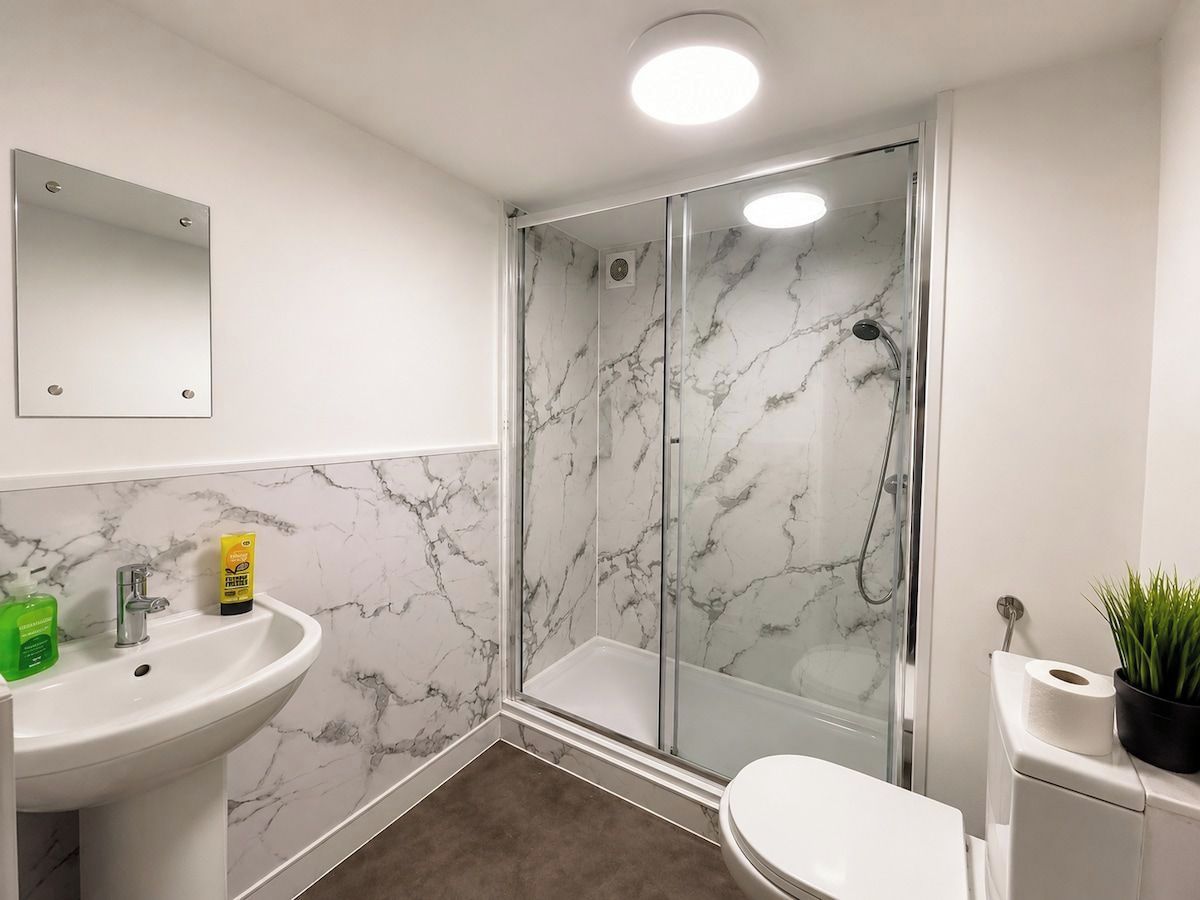Un baño con pared de mármol, cabina de ducha de cristal, lavamanos y retrete.