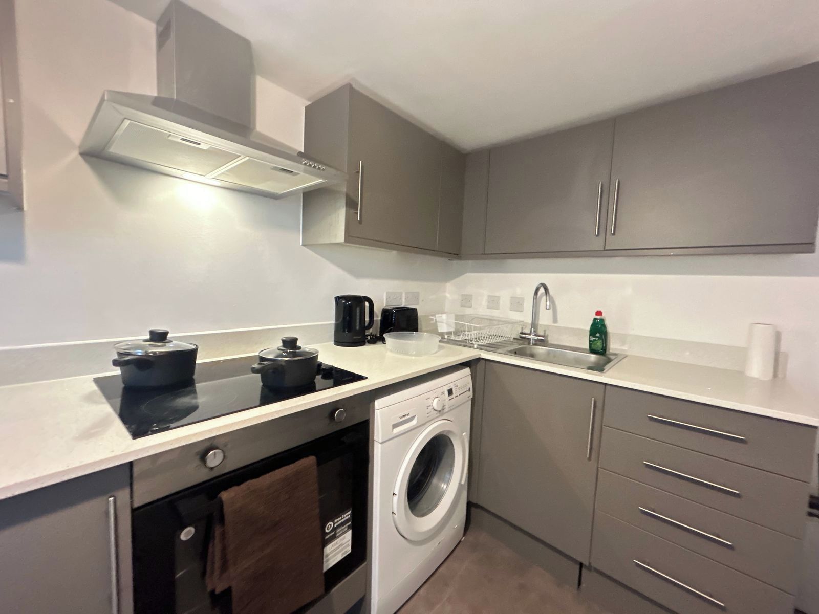 A compact kitchen with a built-in oven, a washing machine, and a coffee maker.