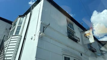 A white building with a black roof, a visible window, and a balcony.