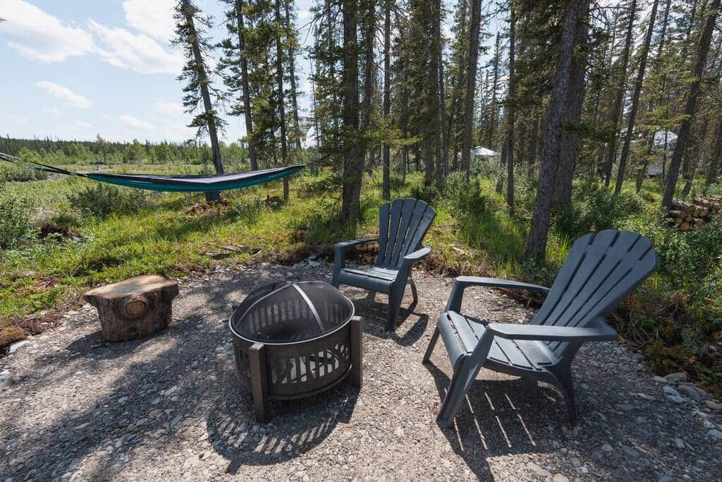 Un terrain de camping équipé d’un foyer, de deux fauteuils Adirondack et d’un hamac.