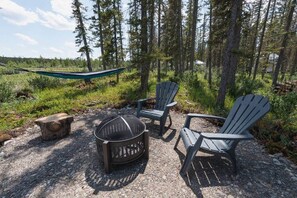 A campsite with a fire pit, two Adirondack chairs, and a hammock.