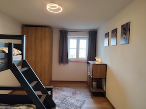 A bedroom with a bunk bed, a desk, a window with curtains, and a ceiling light fixture. - Apartment 'Mair' with Private Terrace, Private Garden and Wi-Fi (Görisried)