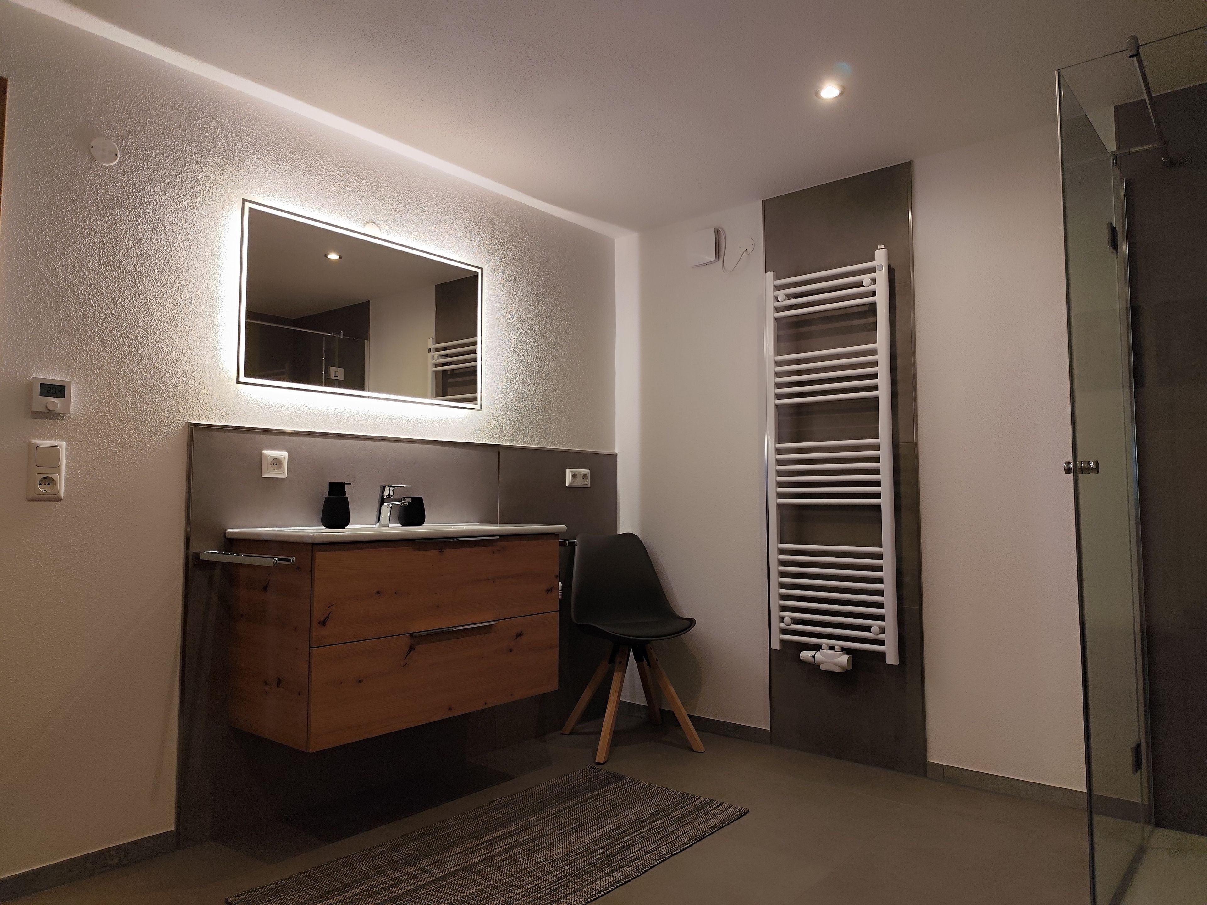 Een badkamer met een houten wastafelmeubel, een spiegel, een handdoekhouder en een douchecabine met glazen wanden.