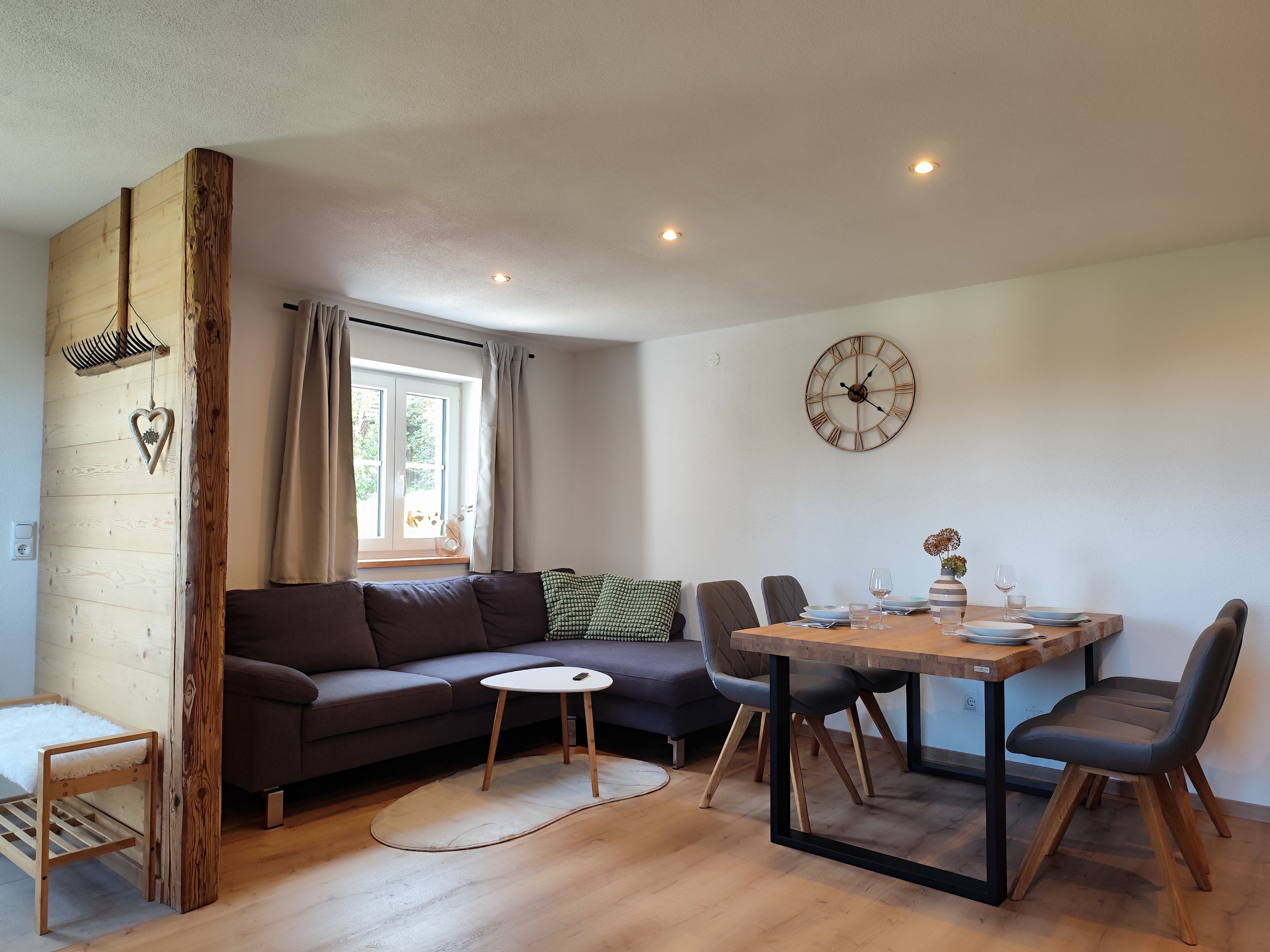 A modern living space with a sofa, dining table, chairs, a clock, and a window with curtains.
