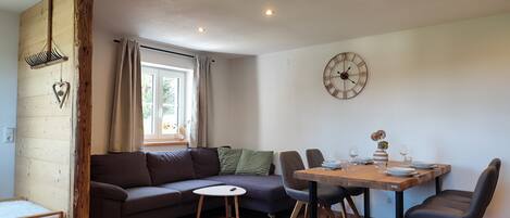 A modern living space with a sofa, dining table, chairs, a clock, and a window with curtains.