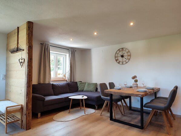 Un espacio habitable moderno con un sofá, una mesa de comedor, sillas, un reloj y una ventana con cortinas.