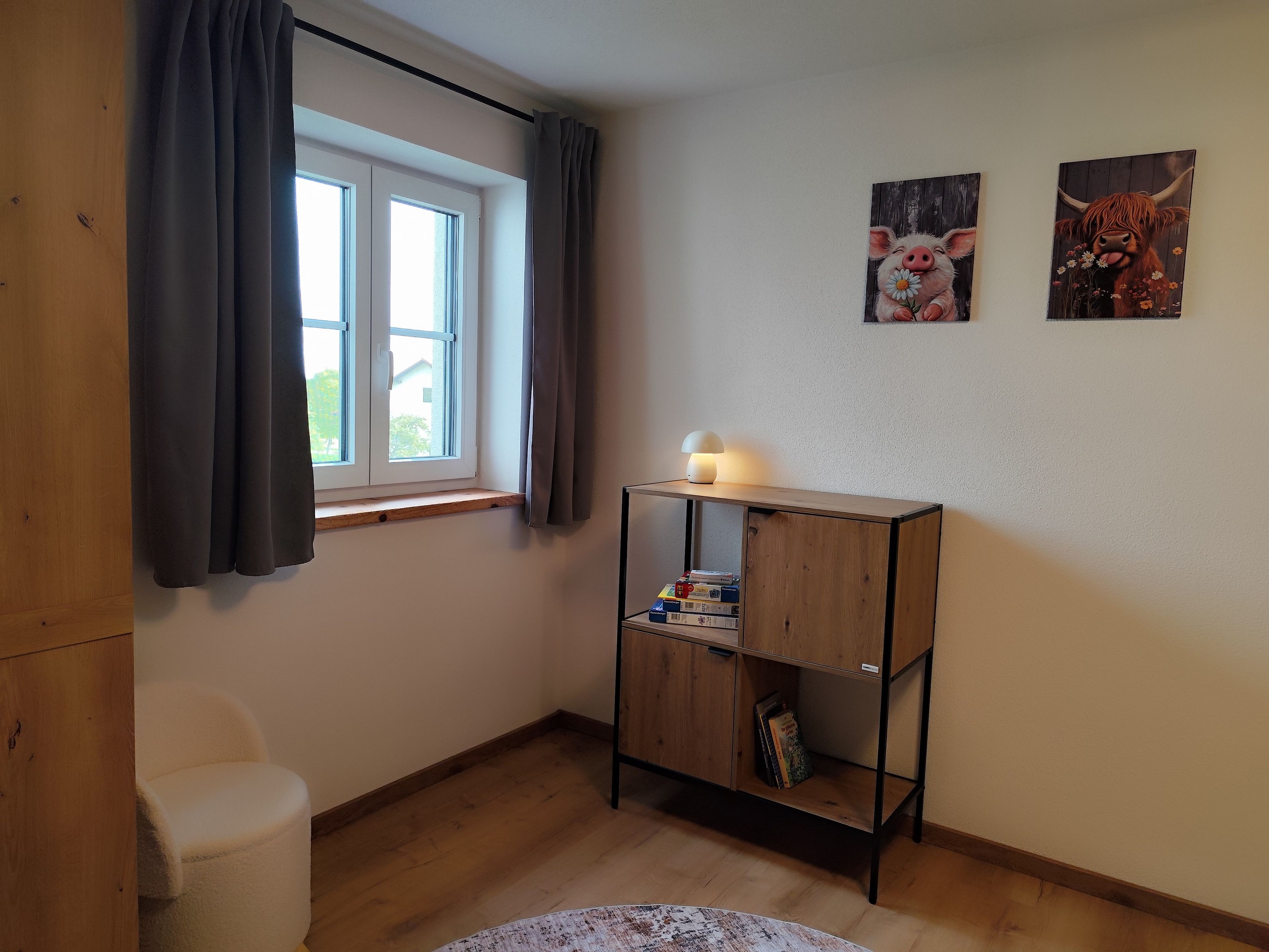 Una habitació amb una finestra, un escriptori amb una làmpada i dos quadres penjats a la paret.