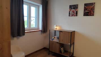 Una habitació amb una finestra, un escriptori amb una làmpada i dos quadres penjats a la paret.