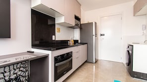 A modern kitchen with a black countertop, white cabinets, a stainless steel refrigerator, and a built-in oven. - Studio in Vila Olímpia with Pool and Gym (São Paulo)