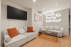 A modern living room with two white sofas, a flat-screen TV mounted on the wall, and a neon sign on the wall. - SmartStay Bird Family Bellecour - Lyon (Lyon)