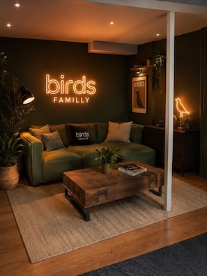 A modern living room with a green sofa, a wooden coffee table, and a neon sign reading 'birds FAMILYLY'. - SmartStay Bird Family Bellecour - Lyon (Lyon)