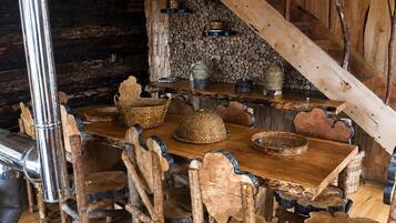 Un comedor rústico con una mesa y sillas de madera, rodeado por una pared de piedra y vigas de madera.