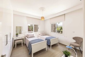 A bedroom with two beds, a desk, a chair, and a window with a view of greenery. - Villa Cecilia Coral - Six Bedroom Villa, Sleeps 12 (Peyia)