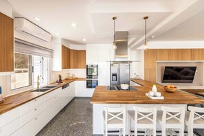 A modern kitchen with a central island, white cabinetry, stainless steel appliances, and a large window. - Villa Cecilia Coral - Six Bedroom Villa, Sleeps 12 (Peyia)