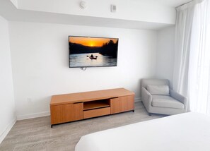 A hotel room with a bed, a TV mounted on the wall, a wooden cabinet, and a light grey armchair. - 2BR Beachwalk Suite Intracoastal & Marina (Hallandale Beach)
