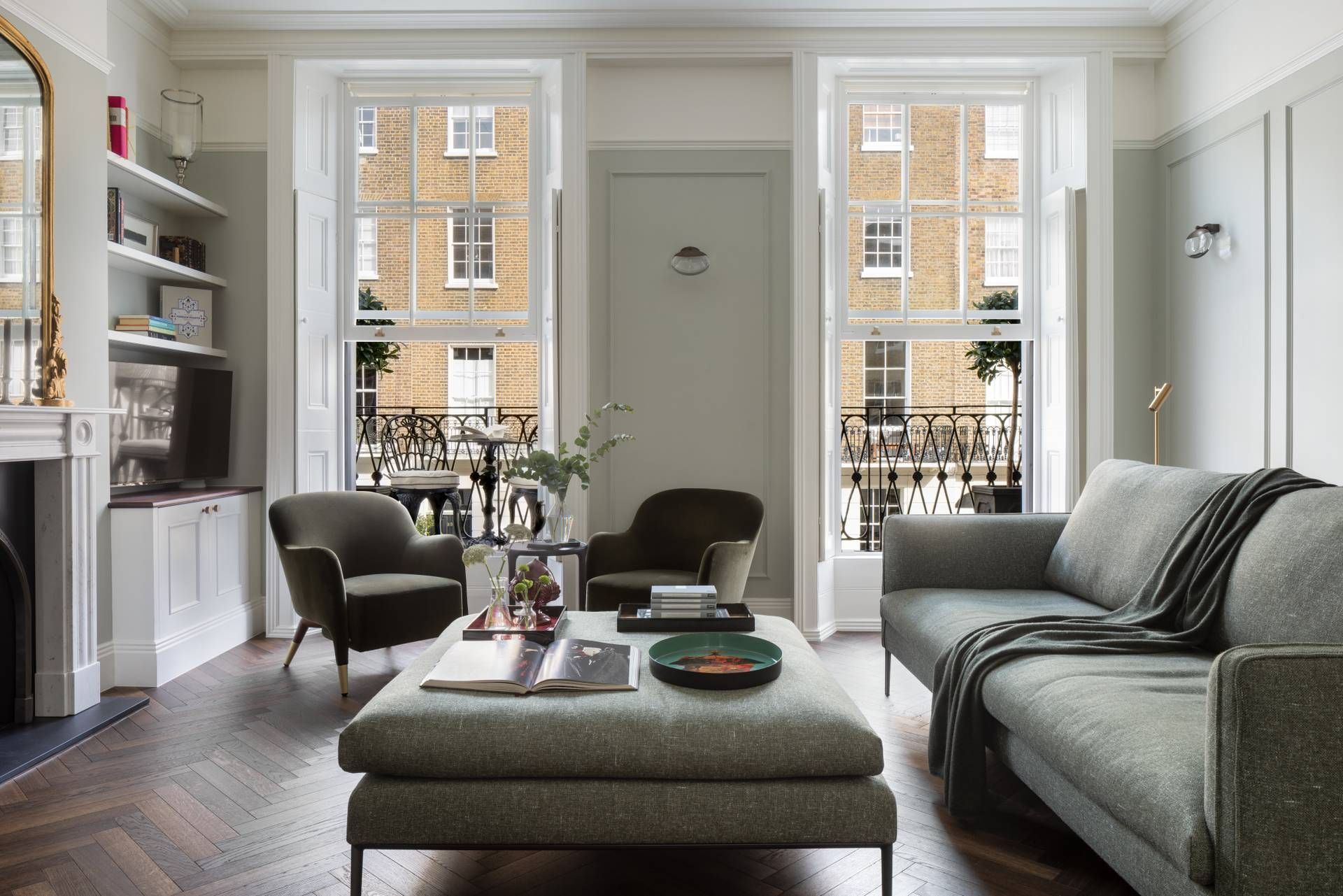 Una sala de estar con sofá, sillón, reposapiés, chimenea y estantería.