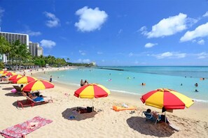 Ein Strand mit Sonnenschirmen, Liegestühlen und badenden Personen.