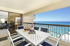 Ein Balkon mit Esstisch, der Blick auf das klare, blaue Meer mit Booten bietet.
