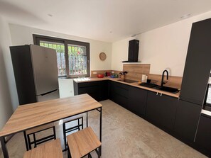 A modern kitchen with a wooden table and chairs, a built-in sink, and a window with a view of greenery. - Spacious Air-Conditioned Villa, 5 Minutes from the Beach (Valras-Plage)