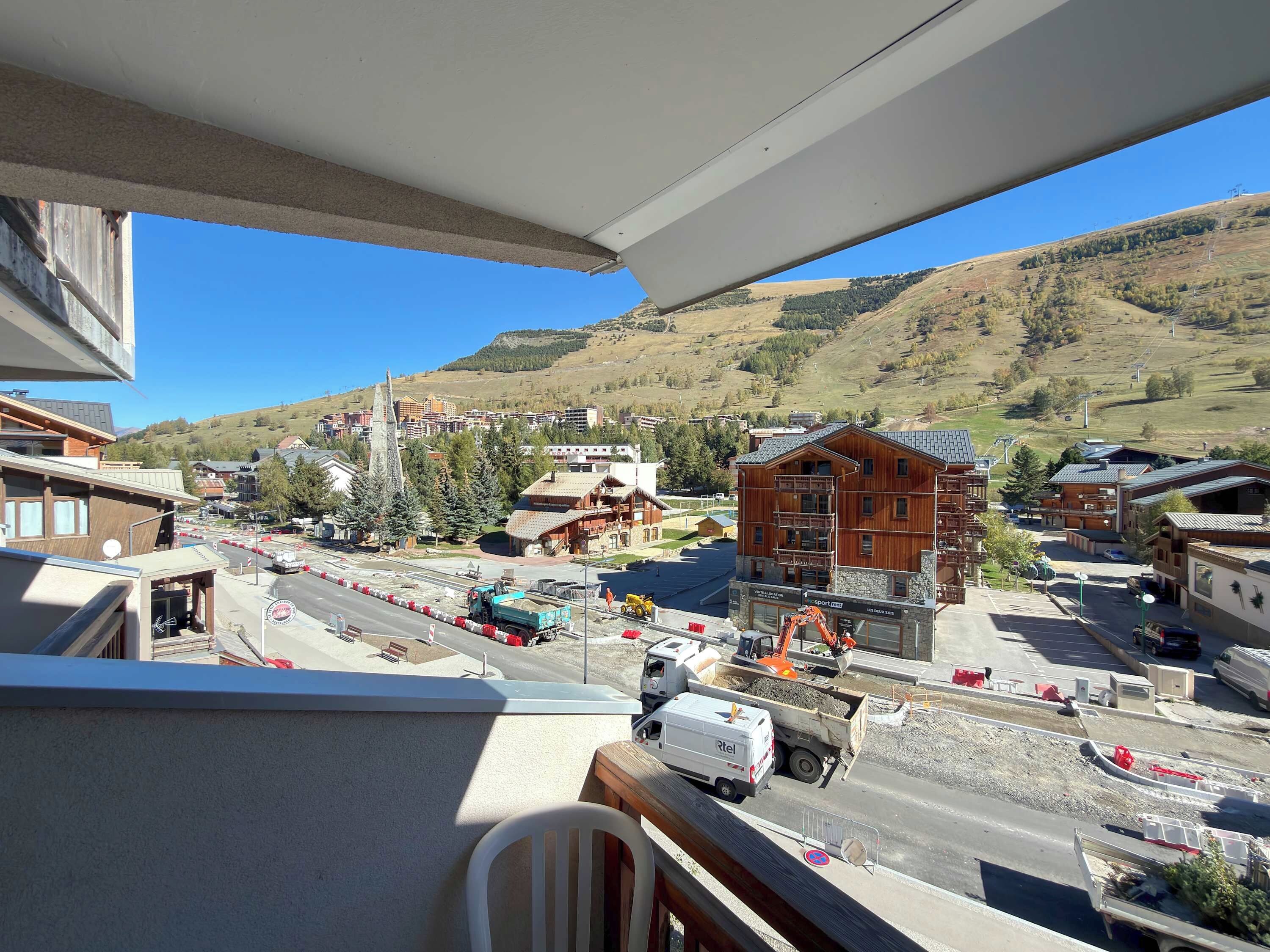 Vista di una città con edifici in legno e moderni, un cantiere edile con macchinari pesanti e un cielo azzurro limpido.