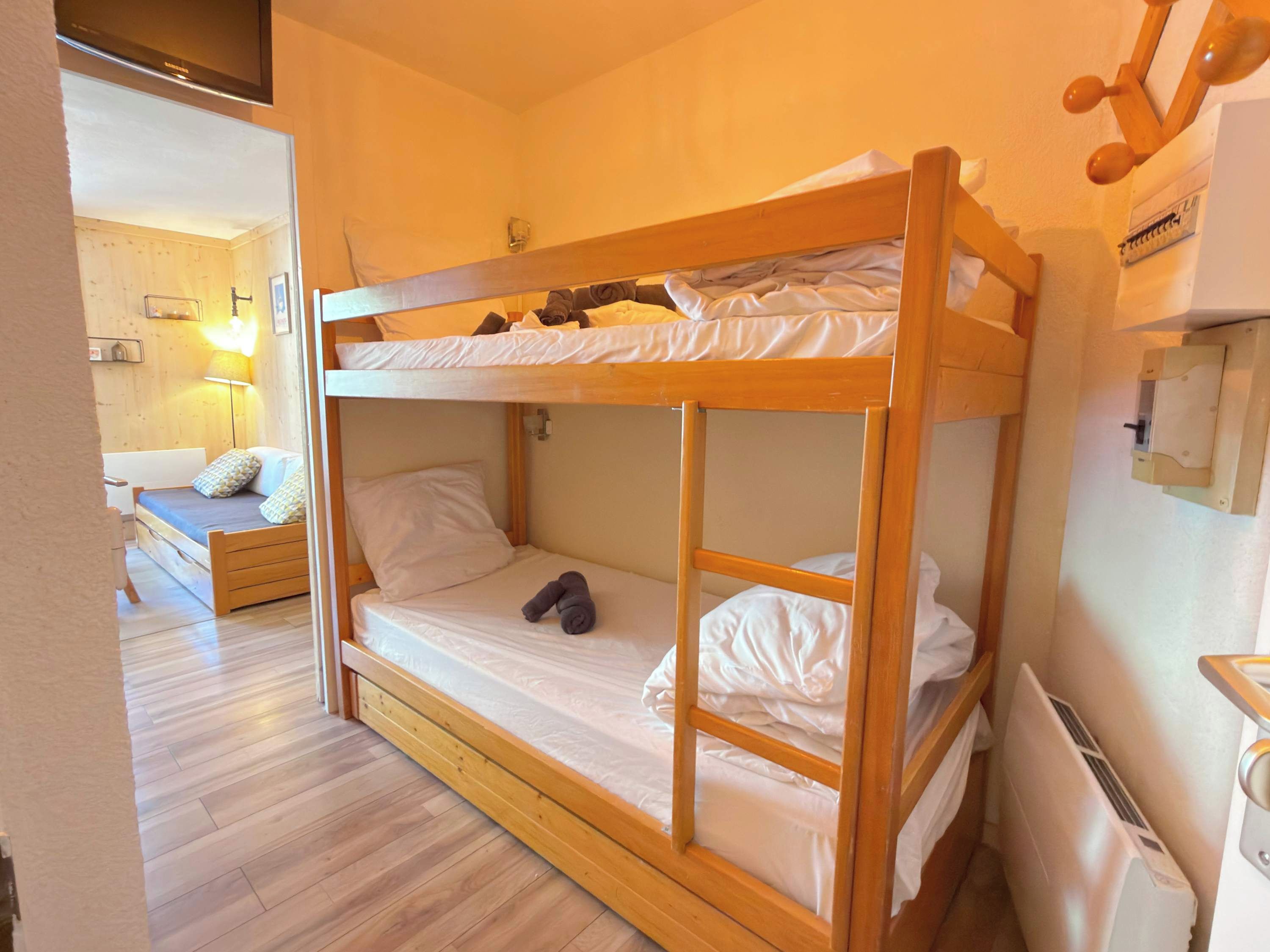 A bunk bed with a lower bunk and a single bed, wooden flooring, a bedside lamp, and a wall-mounted heater.