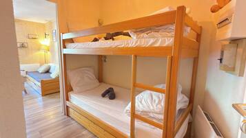 A bunk bed with a lower bunk and a single bed, wooden flooring, a bedside lamp, and a wall-mounted heater.