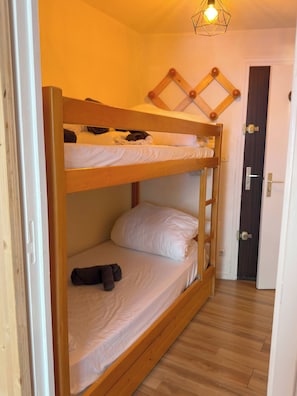 Ein Schlafraum mit Etagenbetten, Holzboden, einer Tür mit Griff und einer Wandleuchte.