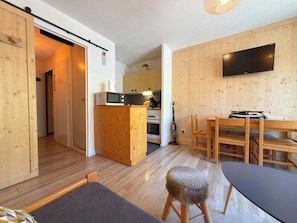 Ein kompakter Wohnraum mit Küchenzeile, Essbereich und an der Wand befestigtem Fernseher.
