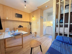 Ein gemütlicher Raum mit Holzvertäfelung, einem Esstisch, einem einzelnen Stuhl, einem Bett mit blauer Decke und einer Küchenzeile.