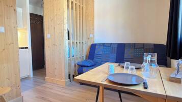 A modern room with a wooden floor, a dining table with chairs, a sofa, and a kitchen area visible through a wooden partition.