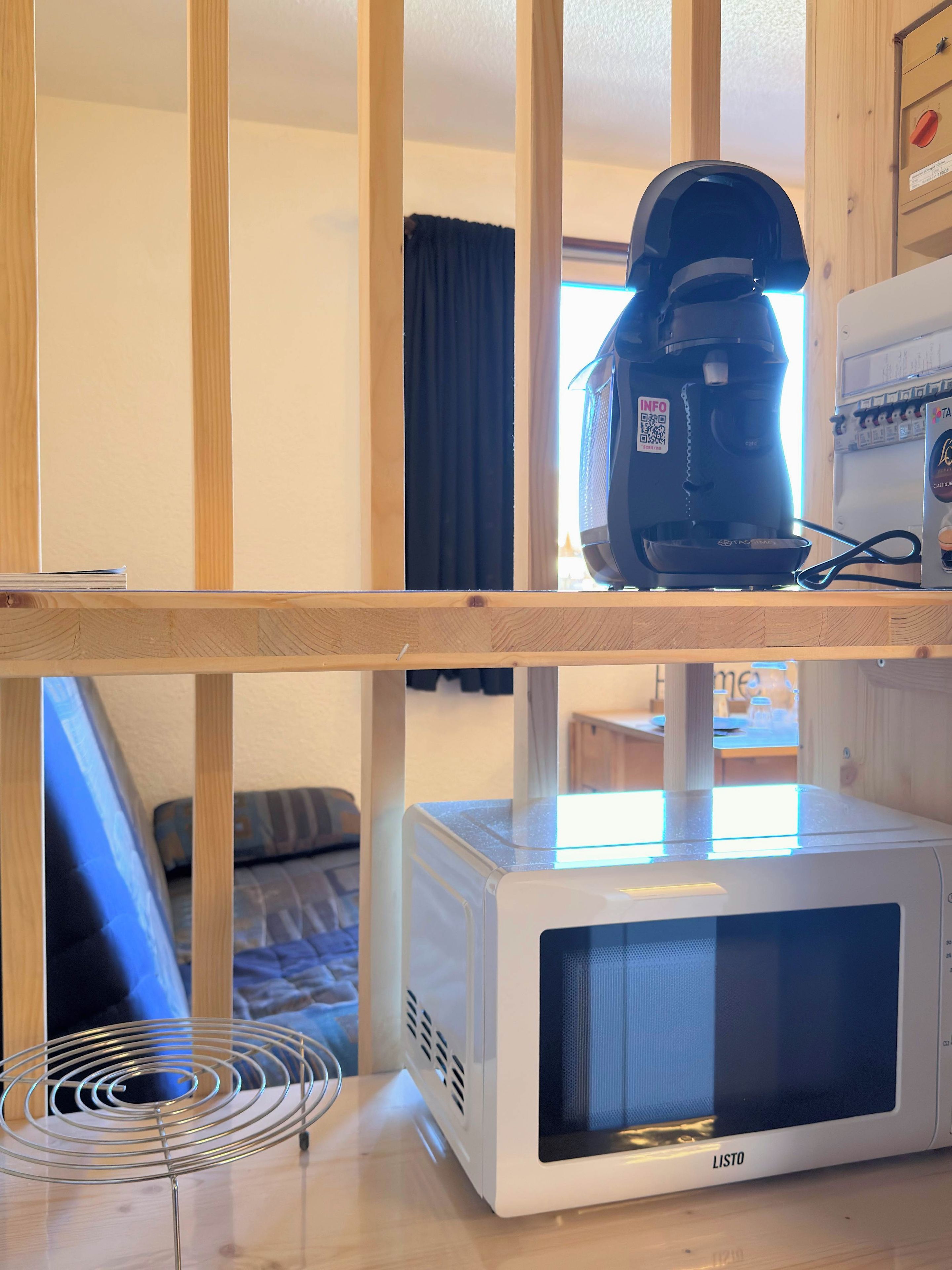 A kitchen area with a microwave, a coffee maker, and a metal rack.