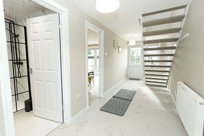 Un couloir avec une porte blanche, un espace douche et un escalier doté d’une rampe à rayures.
