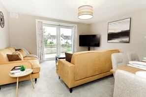 A living room with a sofa, a coffee table, a TV, and a painting on the wall. - The Forest Mews - 3 Bed Cottage Dalbeattie (Dumfries and Galloway)