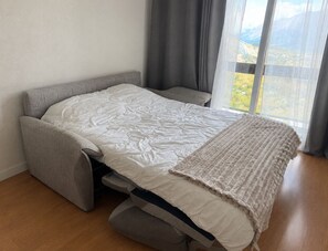 A convertible sofa bed with a white cover, grey cushions, and a view of a mountainous landscape through a large window. - Le Perchoir du Bonheur - Balcon avec vue montagne (Villarembert)