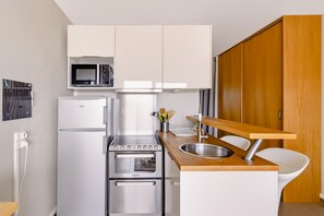 A compact kitchen with a microwave, refrigerator, oven, and a wooden countertop with a sink. - Le P'tit Trez - Vue mer avec parking privé (Benodet)