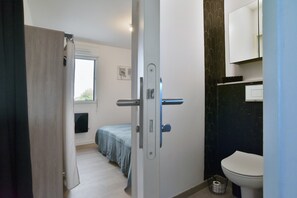 A bedroom with a bed, a door, a window, and a bathroom with a toilet. - L'Instant Émeraude - One Bedroom Apartment, Sleeps 2 (Dinard)