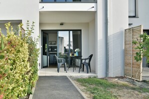 A modern outdoor patio with a table and chairs, a glass door entrance, and a view of the interior. - L'Instant Émeraude - One Bedroom Apartment, Sleeps 2 (Dinard)