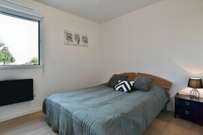 A bedroom with a bed, a nightstand, a lamp, a window, and wall art. - L'Instant Émeraude - One Bedroom Apartment, Sleeps 2 (Dinard)